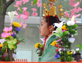 桟敷台に乗る舞姫の少女は少女は天冠をかぶり舞衣に赤い緋袴（ひのはかま）姿